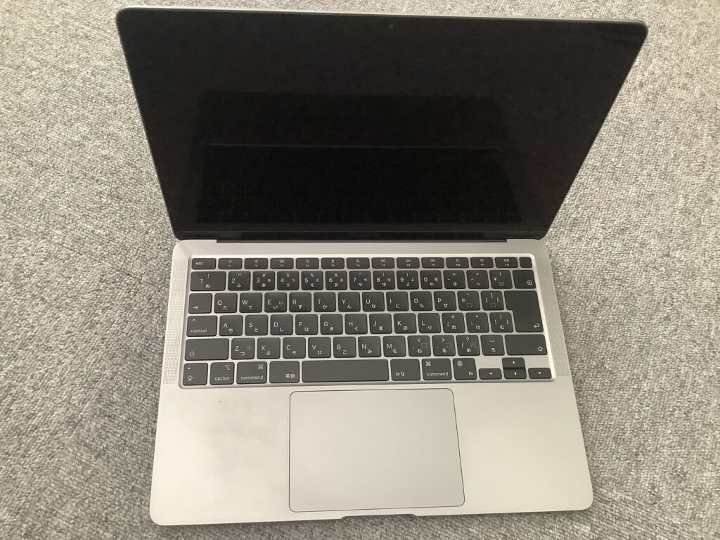 Top-down view of an open silver laptop with a dark screen and black keyboard resting on a textured gray carpet.