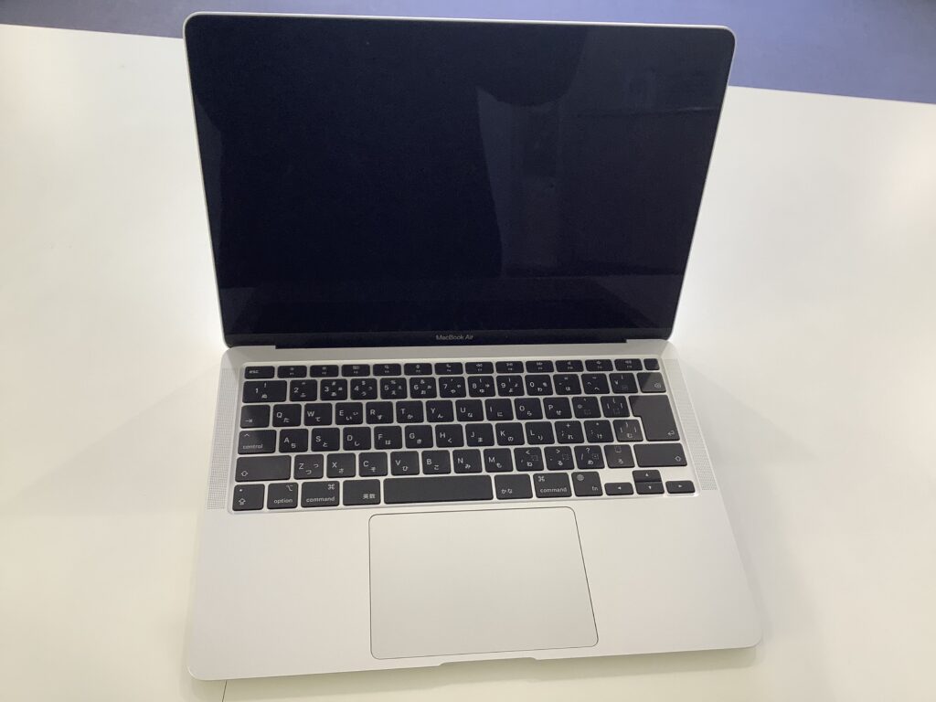 Open MacBook Air on a white desk, screen off, showing silver body and black keyboard with Japanese characters on keys.