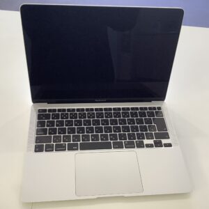 Open MacBook Air on a white desk, screen off, showing silver body and black keyboard with Japanese characters on keys.