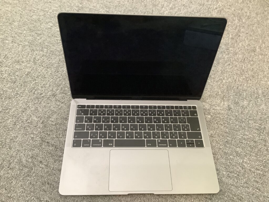 Top-down view of an open silver laptop resting on a gray carpet, the screen is off and keyboard visible.