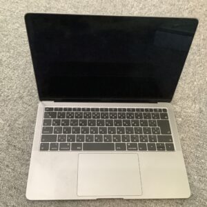 Top-down view of an open silver laptop resting on a gray carpet, the screen is off and keyboard visible.