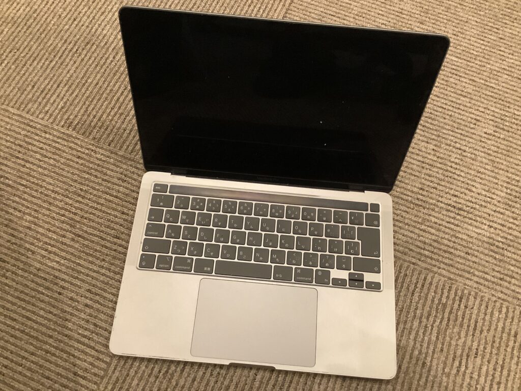 MacbookPro 13 M1 2020 画面割れ 表示不良 | MacからWindowsまでPC買取専門店macsell(マクセル)【ジャンク・故障品】 Open silver laptop with a black screen resting on a beige striped carpet. (informative)