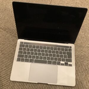 Open silver laptop with a black screen resting on a beige striped carpet. (informative)
